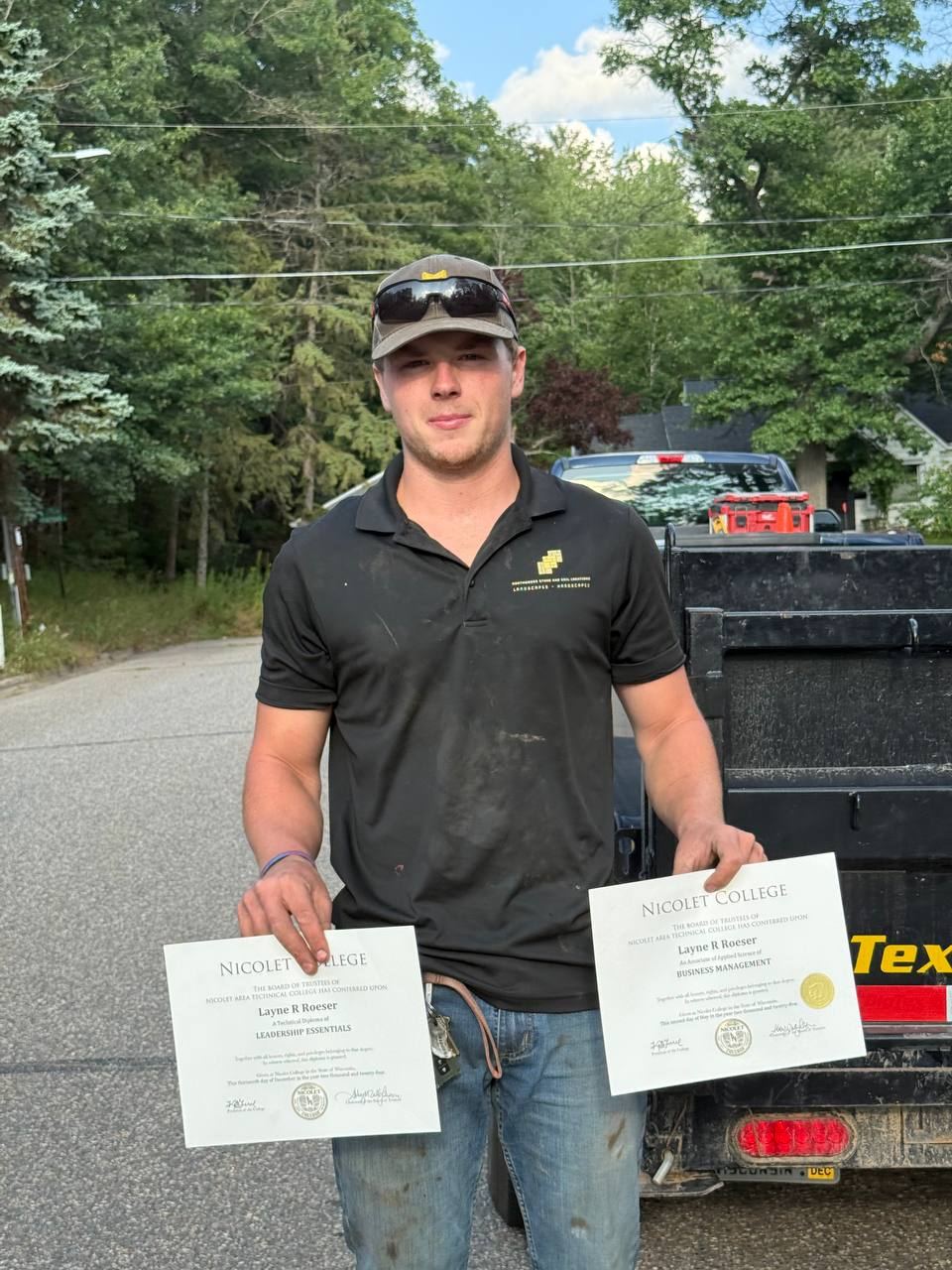 Layne Roeser in his company shirt holding his two Nicolet College degrees